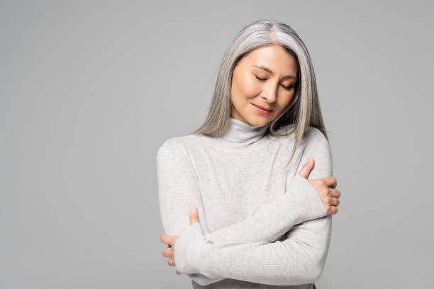 dreamy asian woman in turtleneck with grey hair and closed eyes isolated on grey